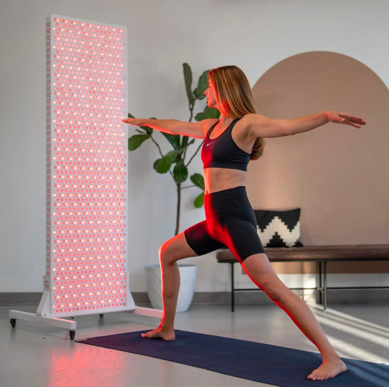 Woman exercising beside a Uray red light therapy panel